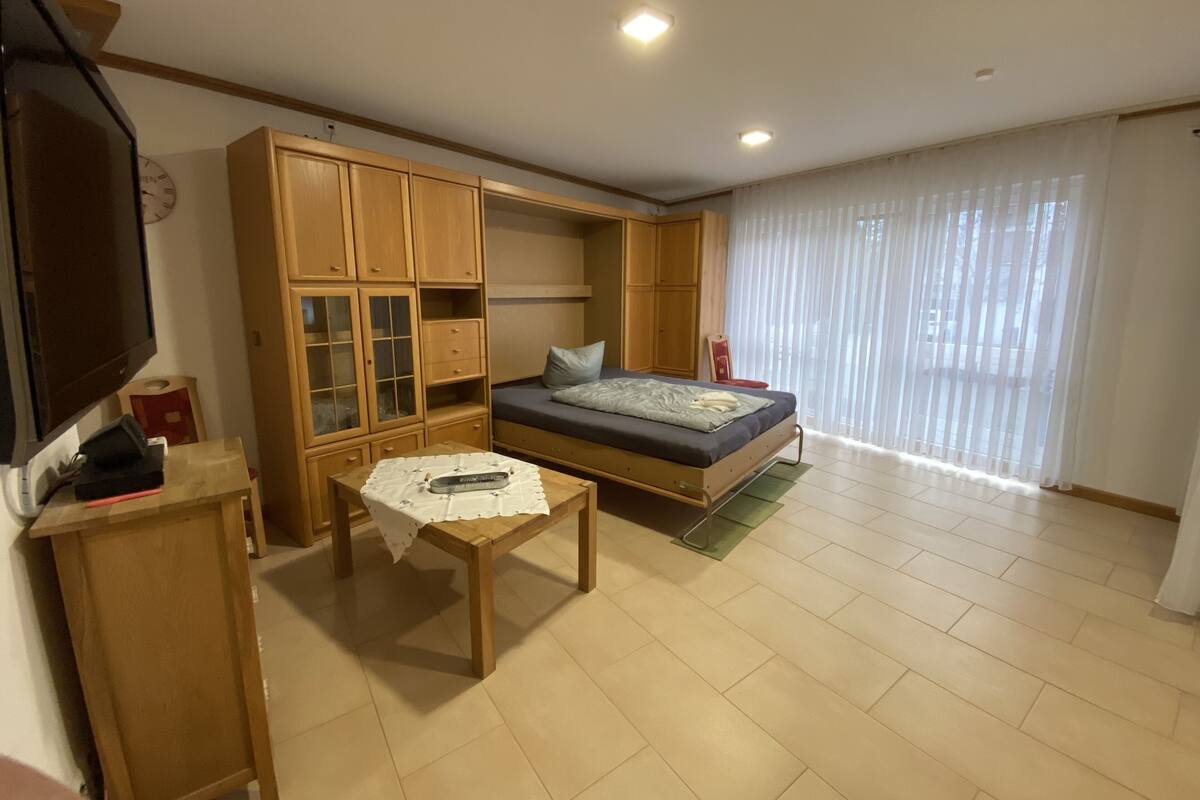 A room with a bed, a wooden cabinet, a small table, and a TV.