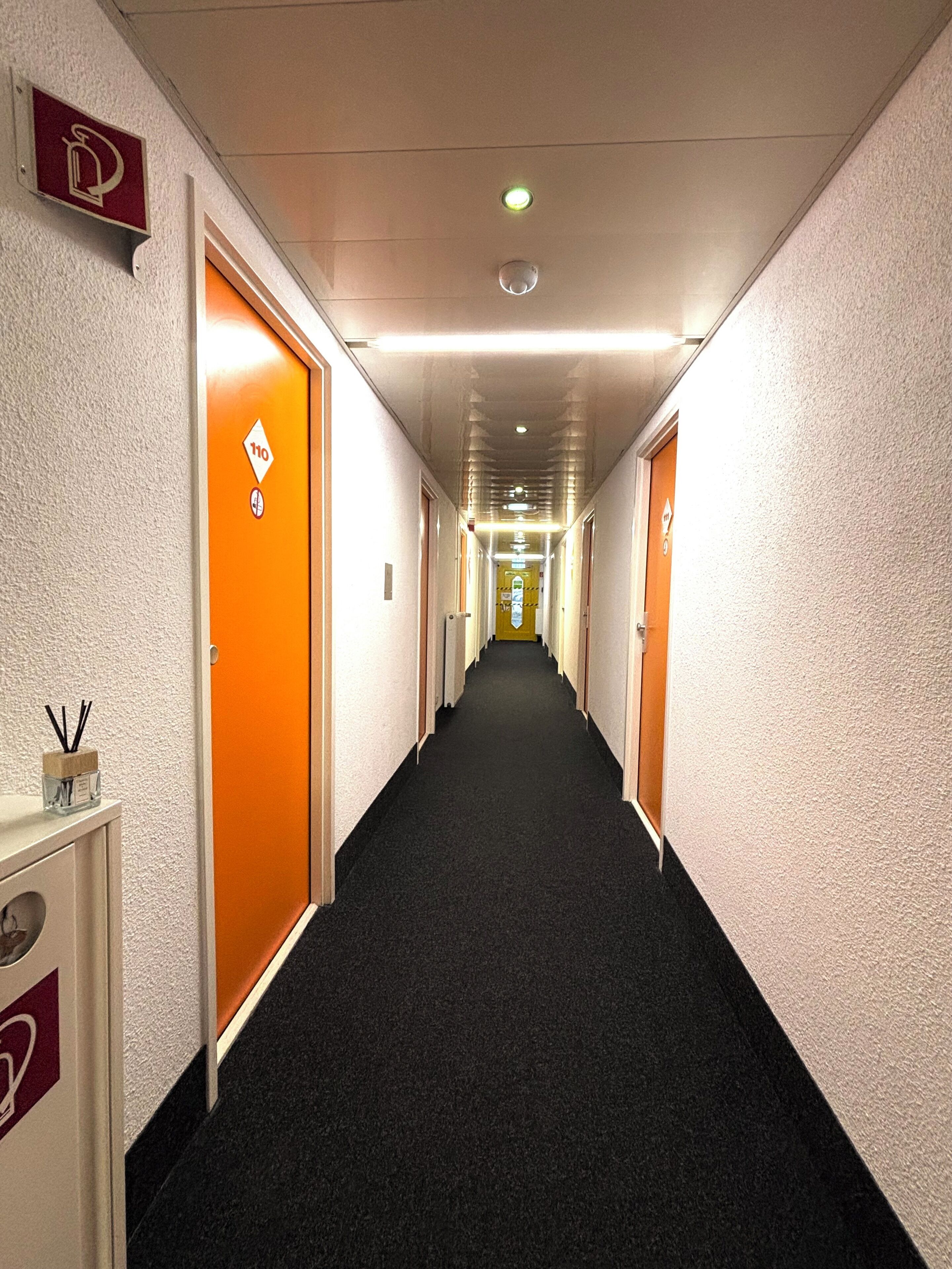 Un couloir d’hôtel avec des portes orange, un détecteur d’incendie et un panneau indiquant un espace réservé aux fumeurs.