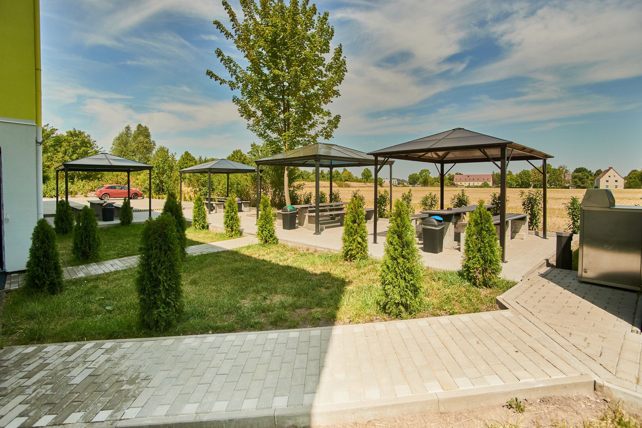 Un patio al aire libre con tres zonas de estar cubiertas, una parrilla y un camino pavimentado.