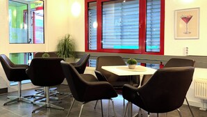 A dining area with a round table, four black chairs, a potted plant, and a window with red frames. - Hotel City Inn Magdeburg (Magdeburg)