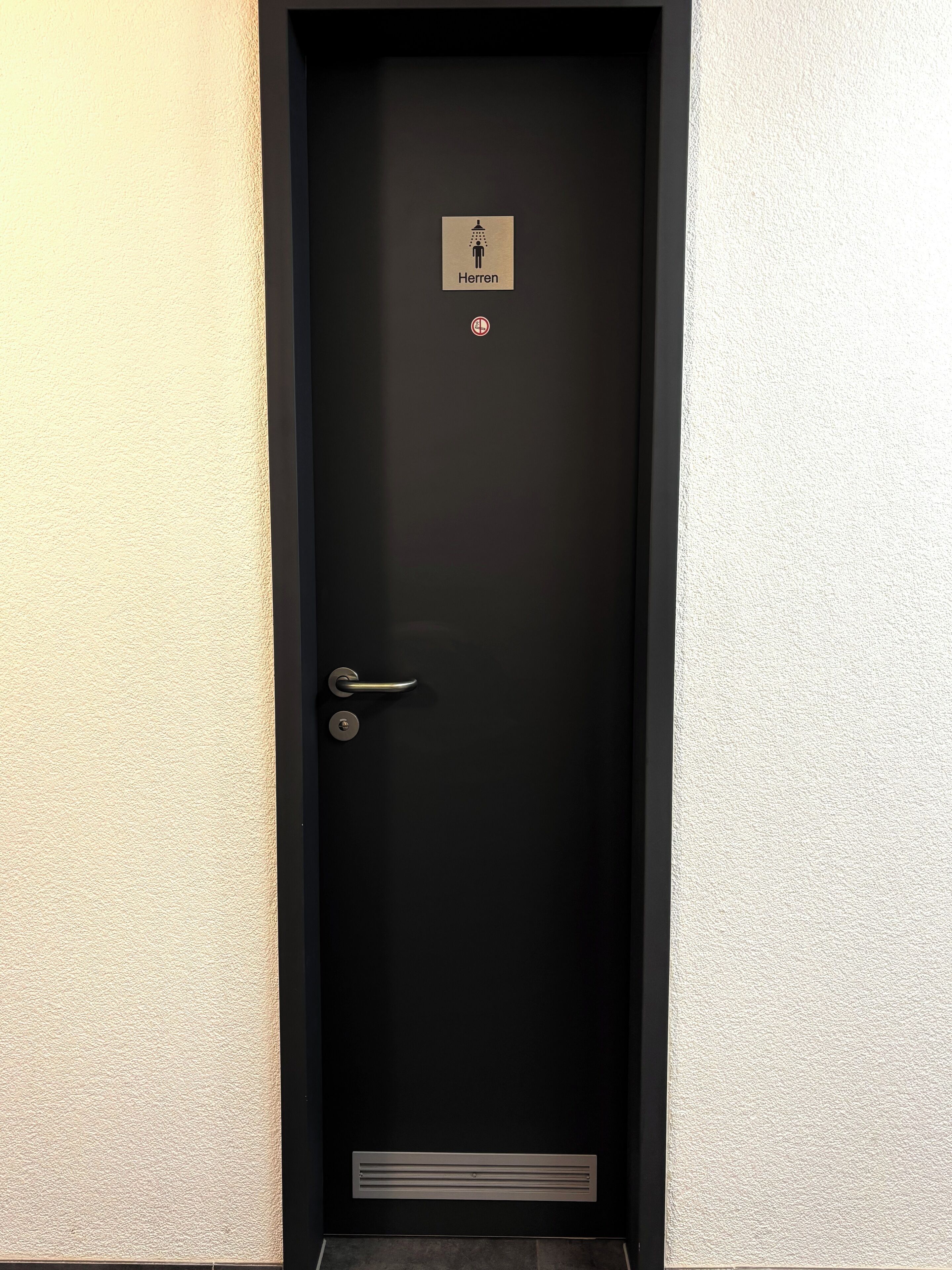 A black door with a sign indicating a men's restroom, a door handle, and a vent at the bottom.