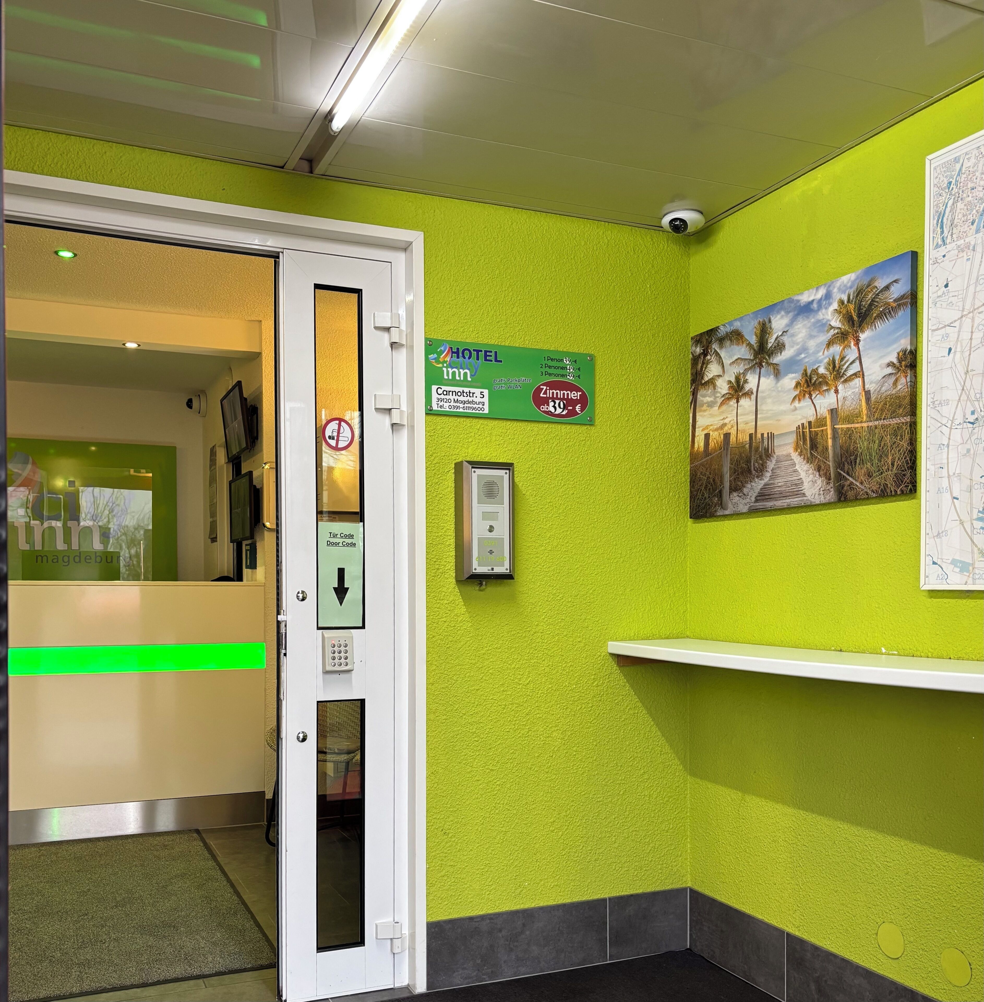 A hotel lobby with a green wall, a painting of a beach, a map, and a sign indicating room rates.