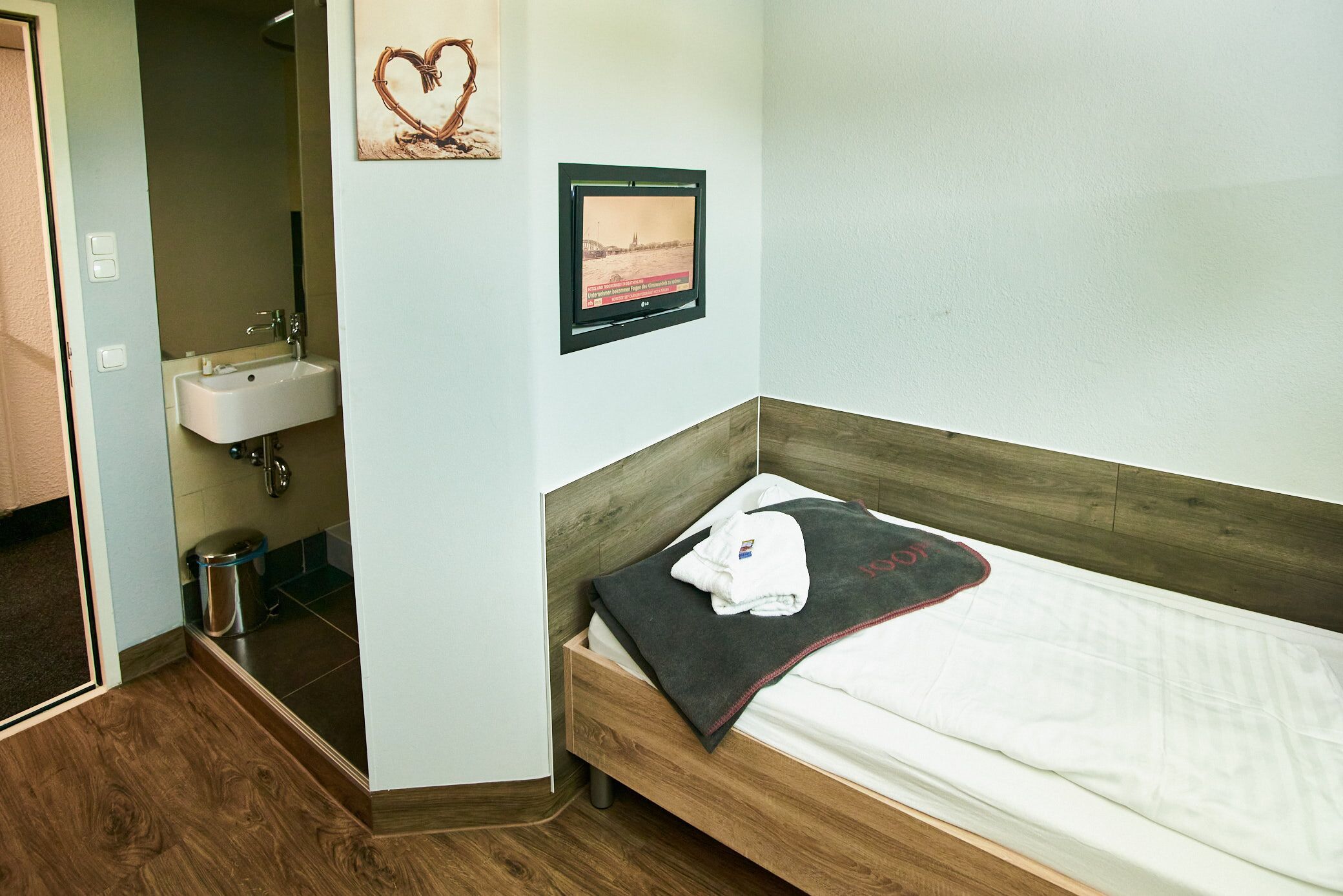 Een hotelkamer met een houten bed, een witte wastafel en een ingelijst schilderij aan de muur.