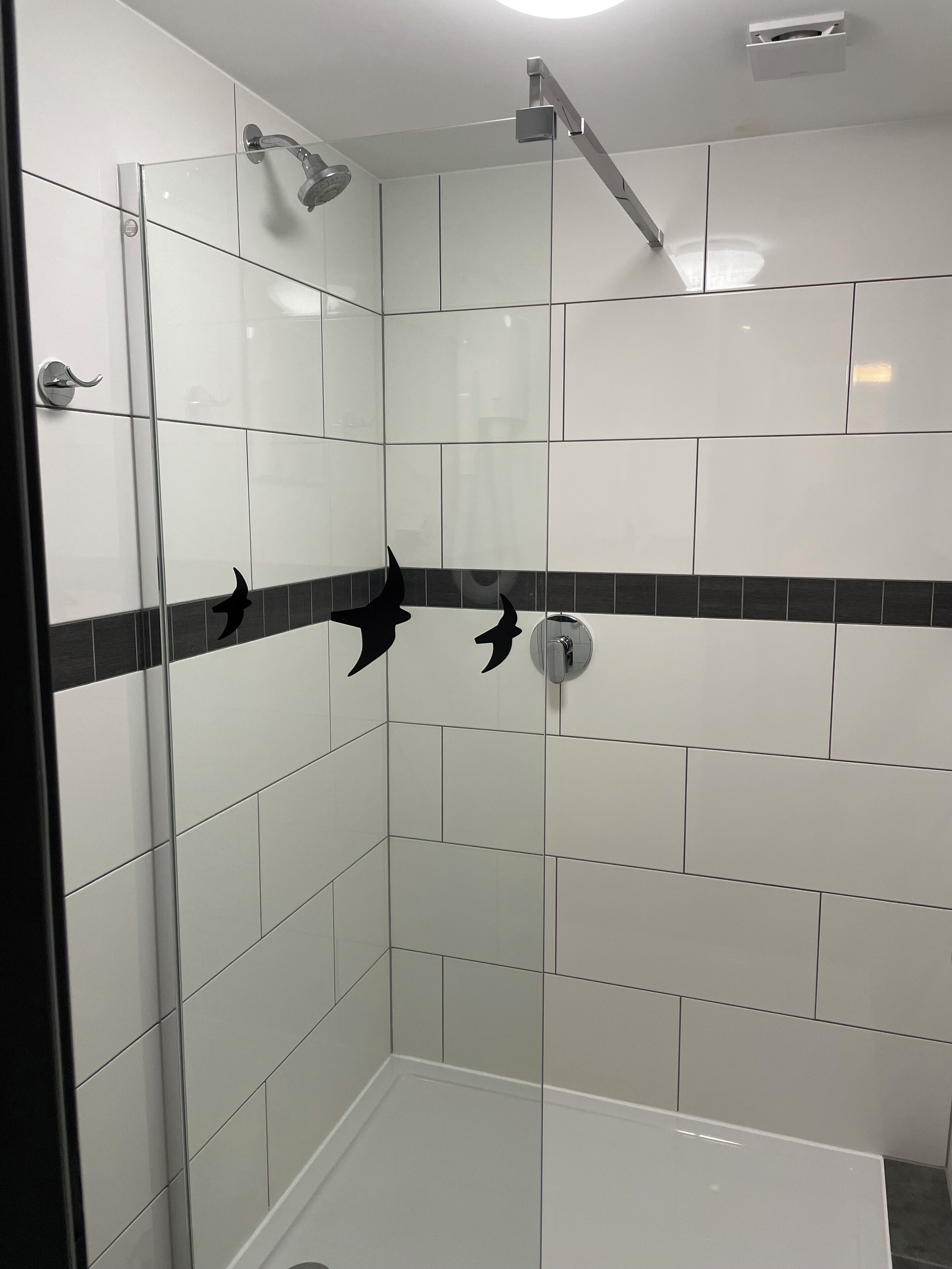 A glass-enclosed shower with white tiles and a black decorative border.