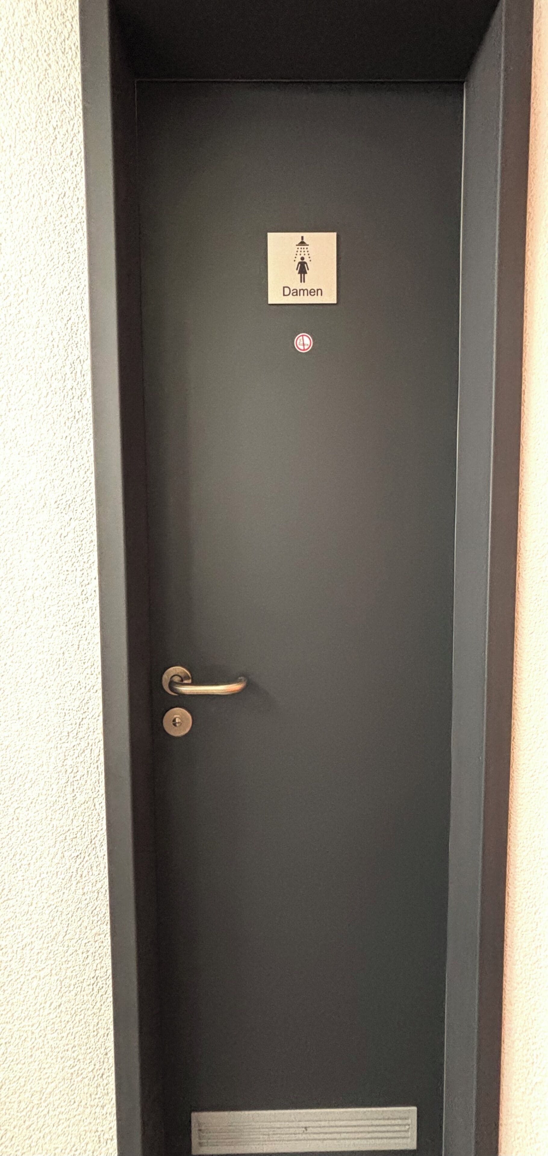 A dark-colored door with a sign indicating a men's restroom and a no-smoking symbol.