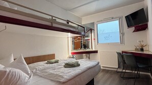 A hotel room with a bunk bed, a desk with a chair, a television, and a window with a view of the sky. - Hotel City Inn Magdeburg (Magdeburg)