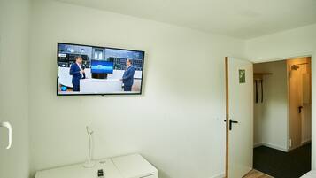 Habitación de hotel con televisión montada en la pared, escritorio con lámpara y puerta que da a otra habitación.