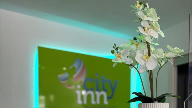A reception desk with a potted orchid, a sign for 'City Inn,' and a green-lit wall. - Hotel City Inn Magdeburg (Magdeburg)