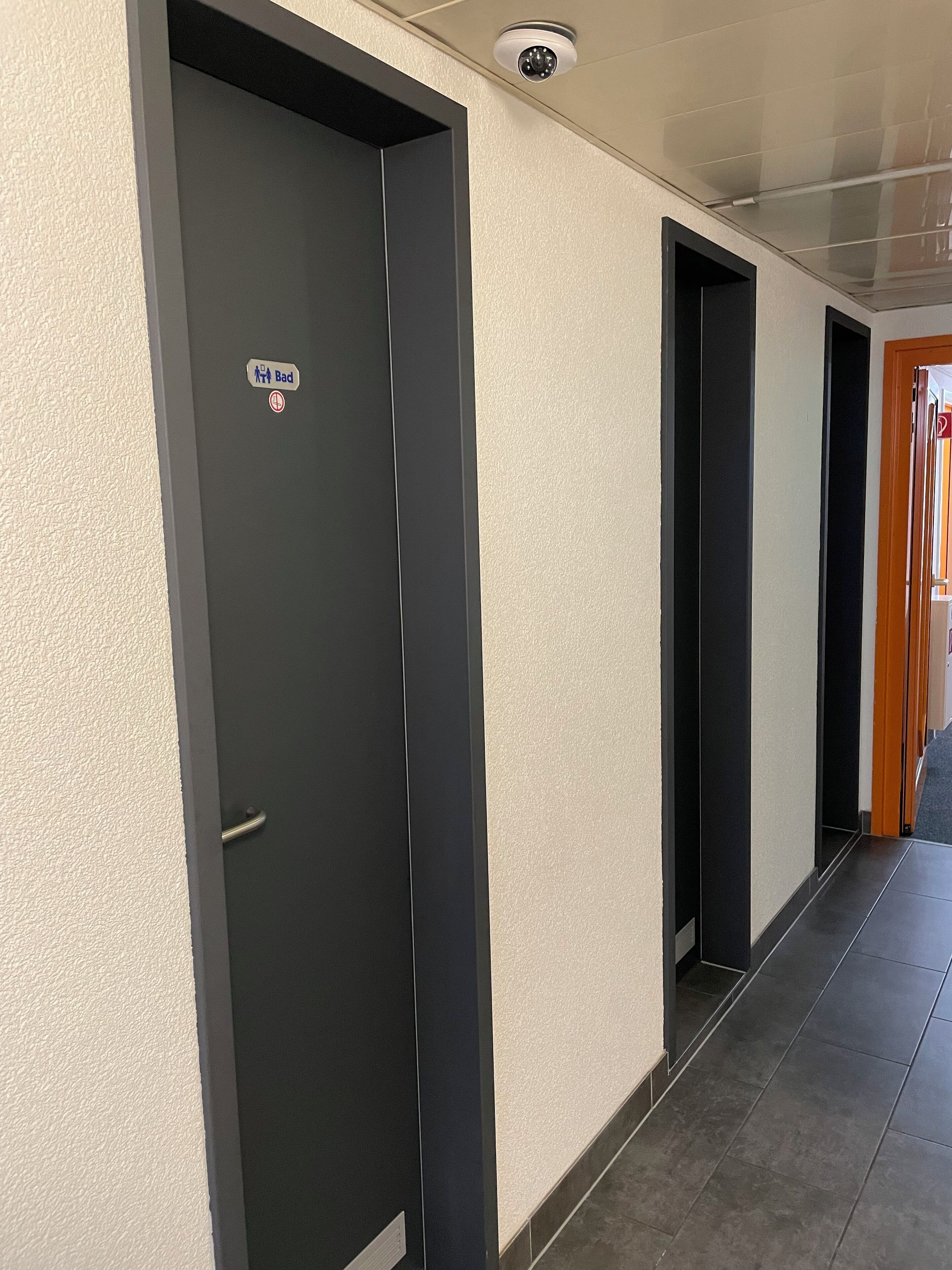 Ein Flur mit schwarzen Türen, einer Überwachungskamera und einem Schild, das einen beschränkten Bereich kennzeichnet.