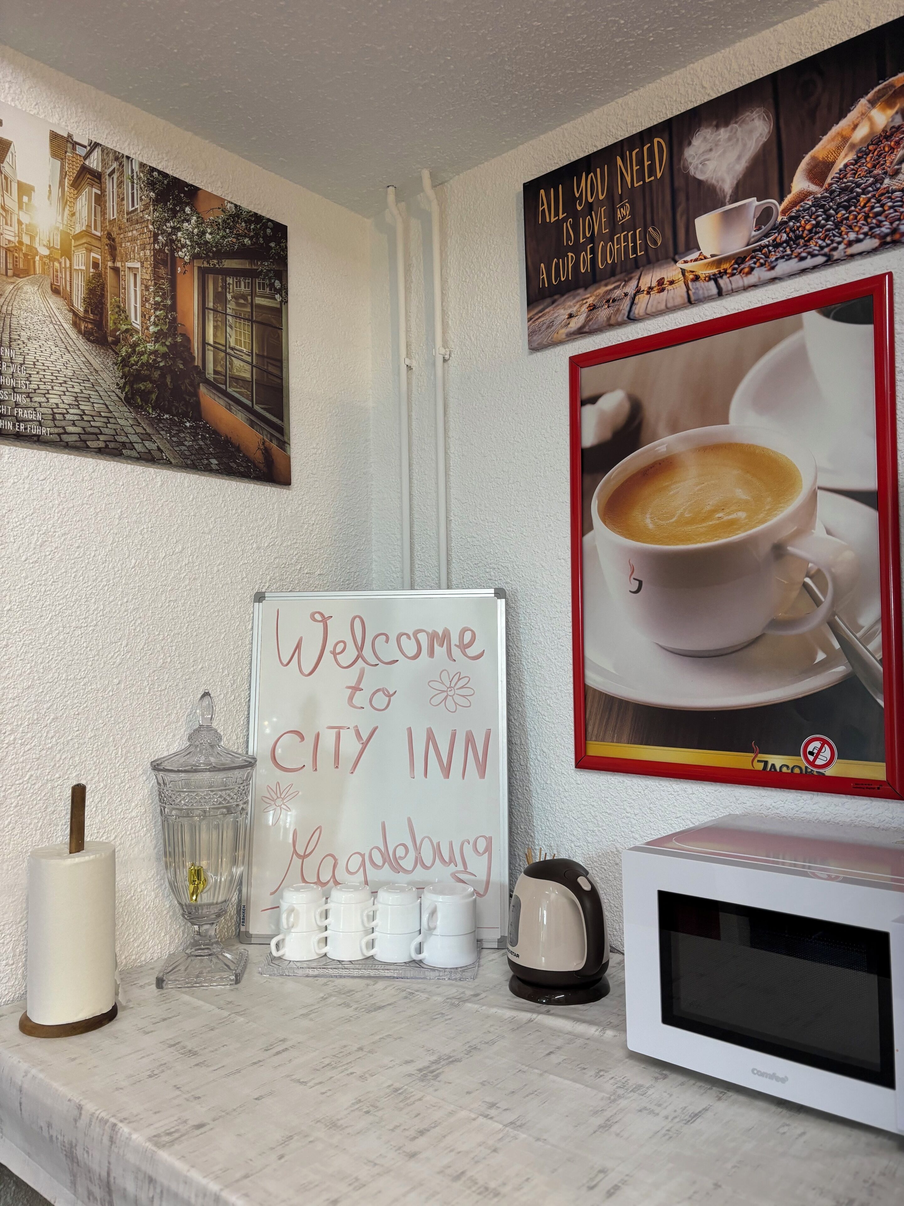 Letrero de bienvenida de una posada urbana, una taza de café, una vela y un microondas sobre una encimera blanca.