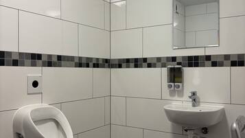 A modern bathroom with white tiles, a urinal, a sink, and a mirror.