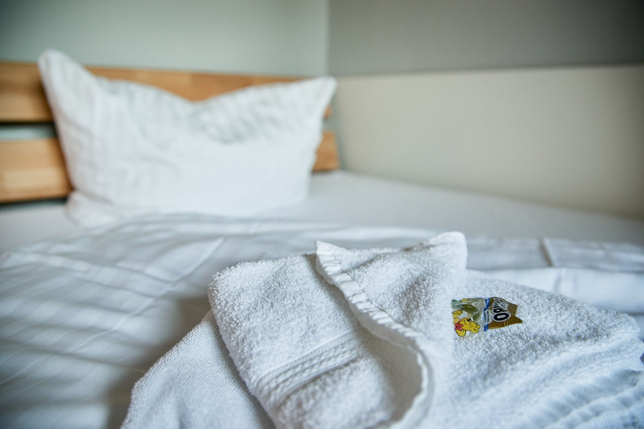 A neatly made bed with white linens and a white bathrobe with a logo on it.