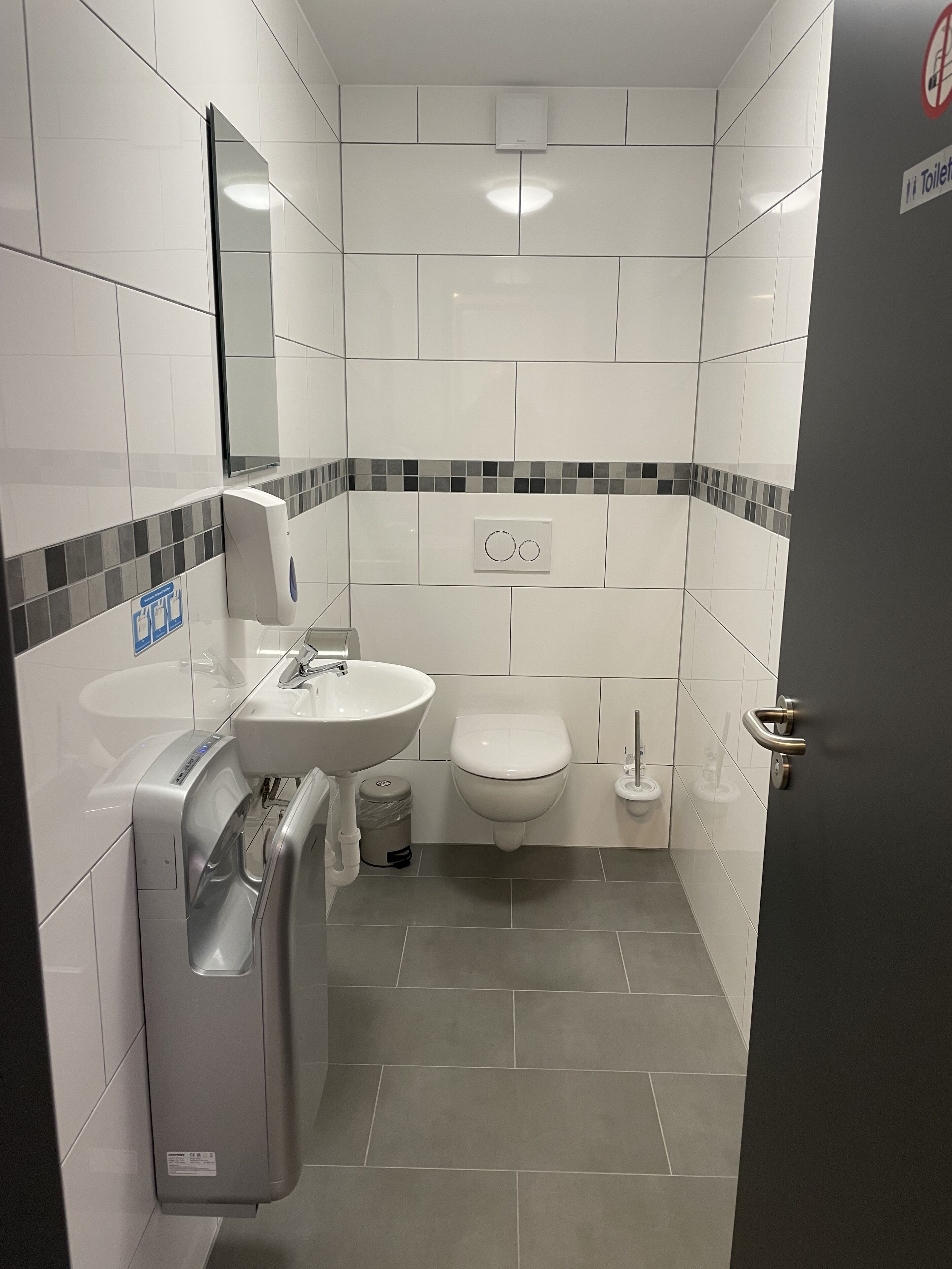 Et lille badeværelse med vask, toilet og håndtørrer.