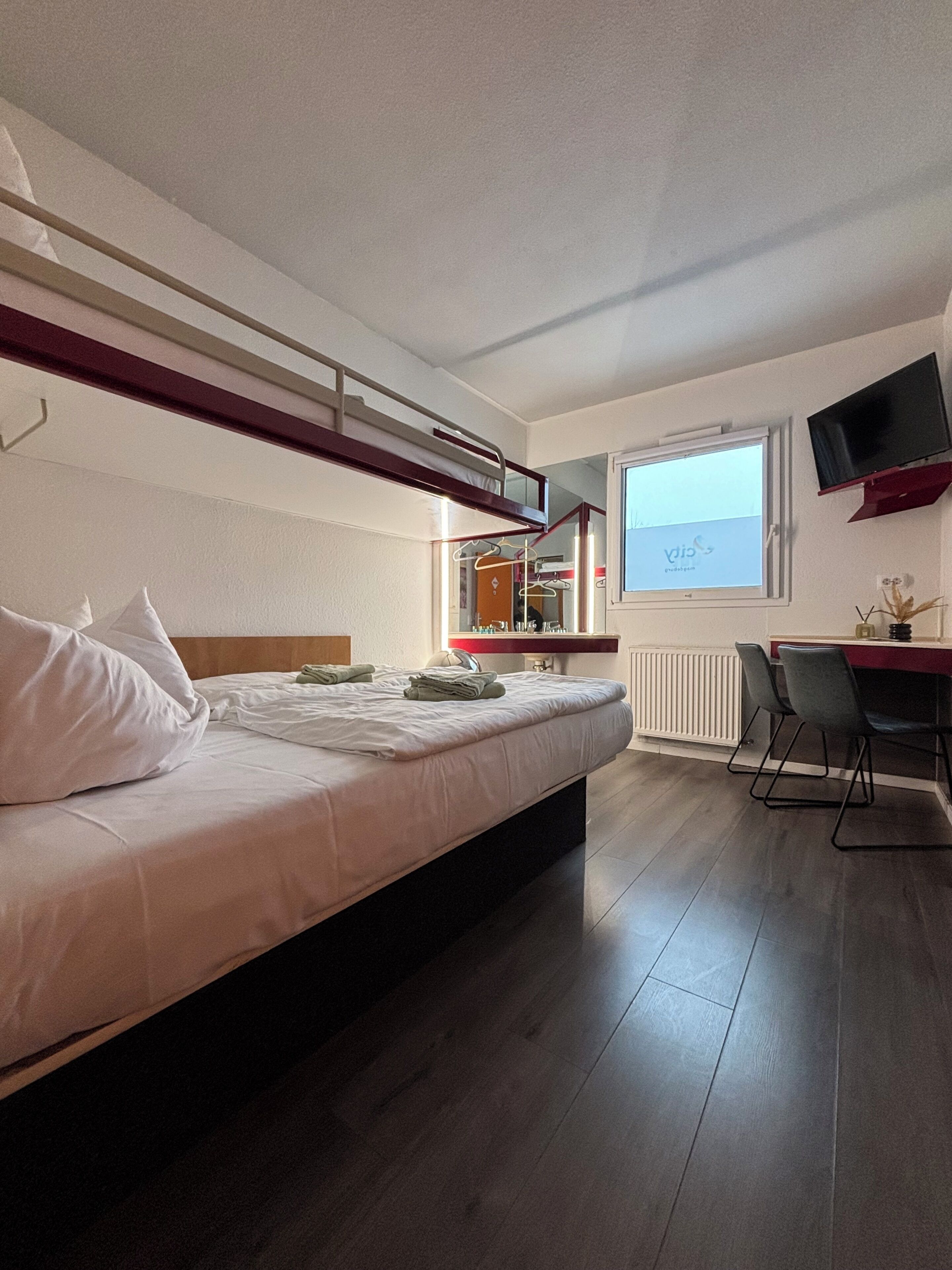 Un dormitorio con literas, un escritorio, una silla, un televisor y una ventana.