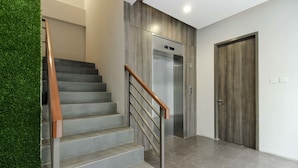 A staircase with a wooden handrail, a wall with a vertical garden, a modern elevator, and a wooden door. - RedDoorz Plus near Tebet (Jakarta)