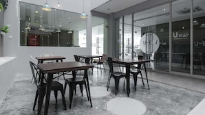A modern hotel lobby with wooden tables and chairs, large windows, and a glass wall with the hotel's name. - RedDoorz Plus near Tebet (Jakarta)