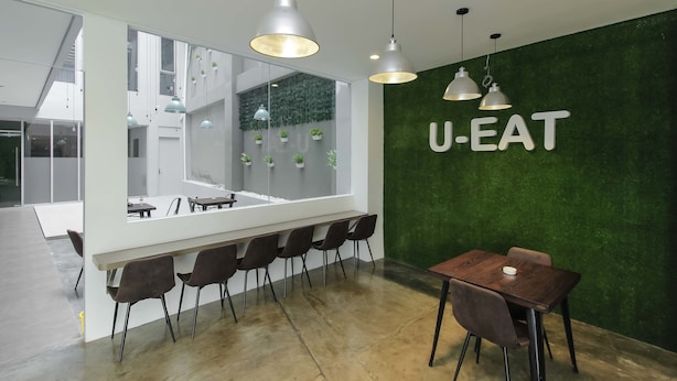 A modern U-EAT restaurant with a green wall, white ceiling, and a wooden dining table. - RedDoorz Plus near Tebet (Jakarta)
