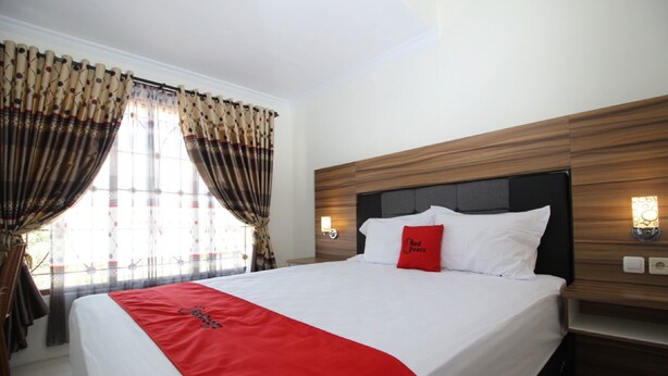 A hotel room with a large bed, wooden headboard, and curtains. - RedDoorz near UGM 3 (Depok)