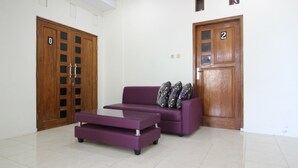 A room with a purple sofa, a glass coffee table, and two wooden doors with numbers. - RedDoorz near UGM 3 (Depok)