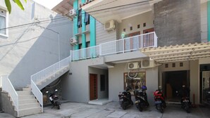 A residential building with a staircase leading to a balcony, multiple parked motorcycles, and a visible door. - RedDoorz near UGM 3 (Depok)