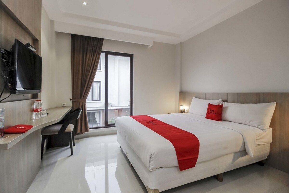 A hotel room with a bed, a desk, a chair, a television, and a window with curtains.