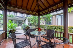 An outdoor covered patio area with wicker furniture, a glass table, and potted plants. - Sans Vibes Jasmine Suite TB Simatupang (Jakarta)