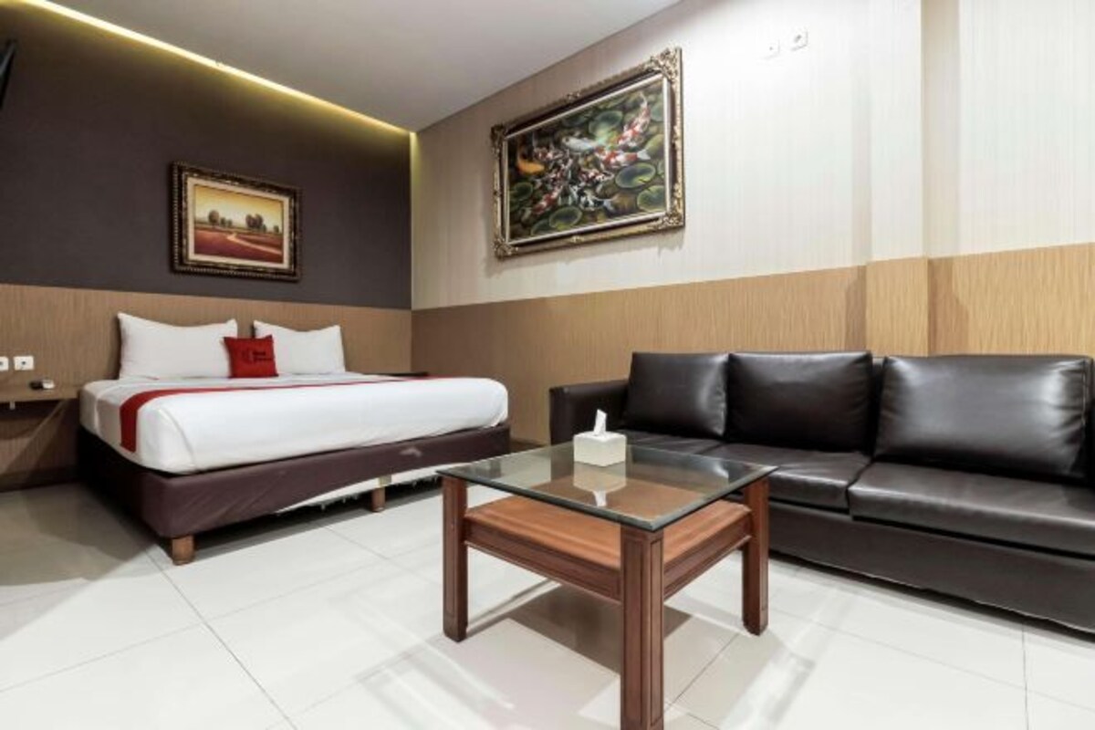 Habitación de hotel con cama, sofá de cuero, una mesita de centro de vidrio y dos cuadros en las paredes.
