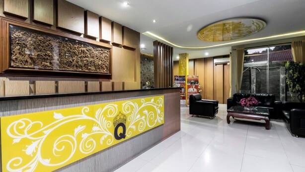 Zona de recepción de hotel con un mostrador de madera, una amplia pared decorativa y un área de estar con sofás negros y una mesa de centro.