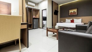 Una habitación de hotel con cama, sofá, una mesita, una silla de mimbre, armario y televisor montado en la pared.