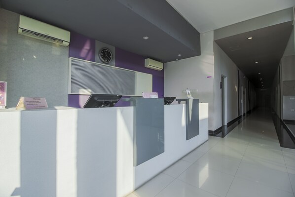 A reception area with a modern design, featuring a reception desk, air conditioning units, and a clock on the wall. - RedDoorz near Goa Sunyaragi (West Cirebon)