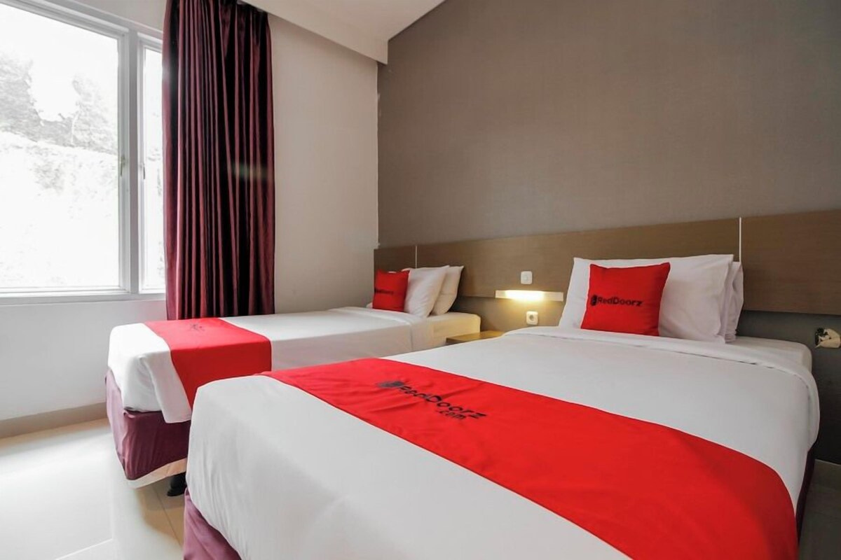 A hotel room with two beds, each with a red and white bedspread, and a window with curtains.