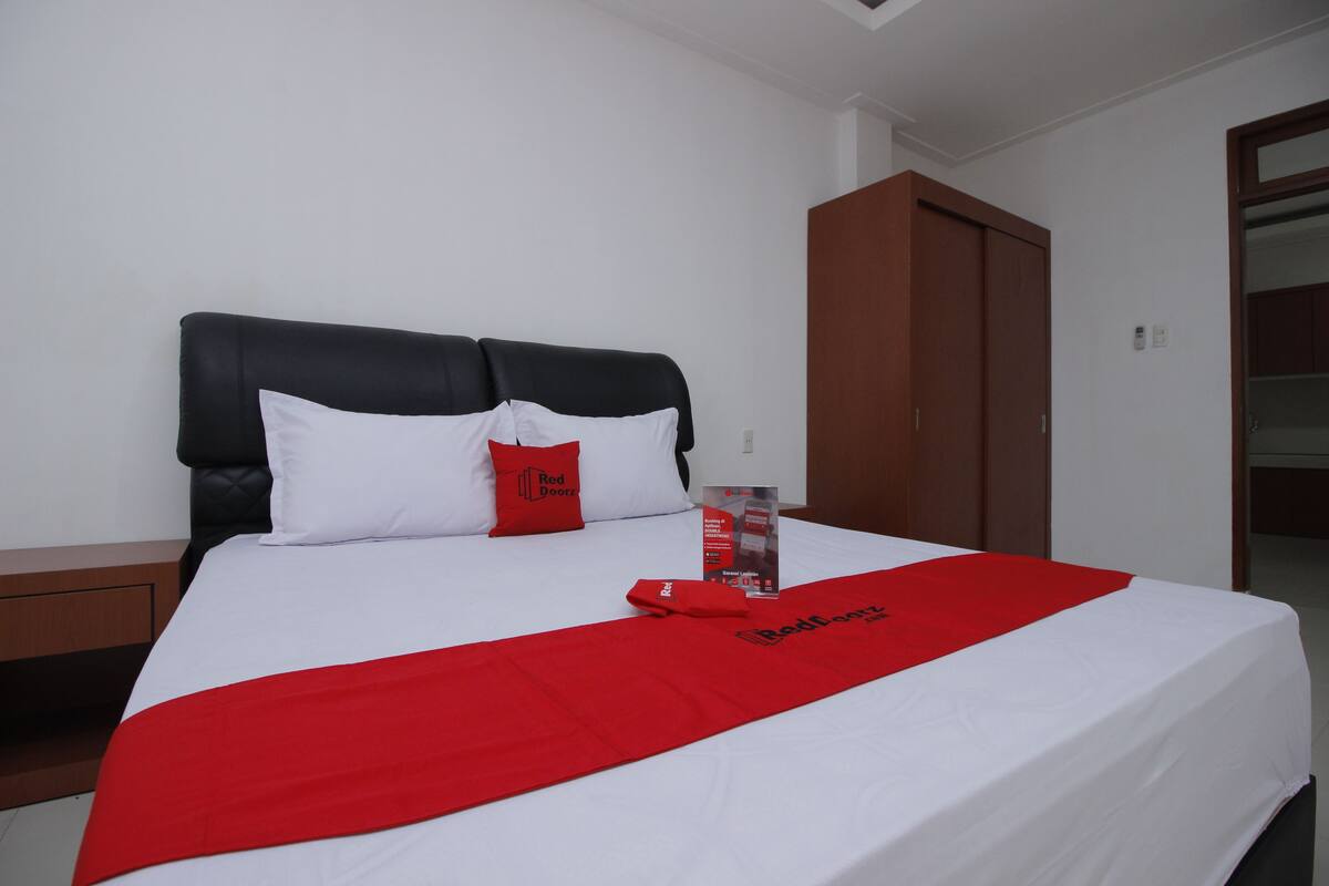 A neatly made bed with a white and red bedspread, a red pillow, and a red blanket with a logo.
