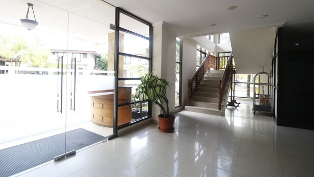 Un vestíbulo espacioso con un amplio ventanal, una planta en maceta, un banco de madera y una escalera que sube a un nivel superior.