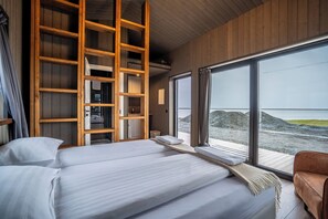 A bedroom with a large window, wooden shelving, and a view of a rocky landscape. - Guesthouse Gerði (Hali)