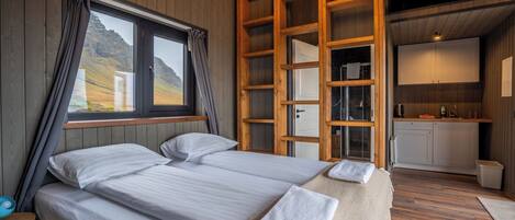 Un dormitorio con dos camas, una escalera de madera, una ventana con cortinas y vistas al exterior, además de una pequeña kitchenette.