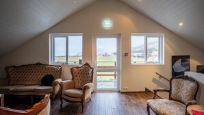 A cozy room with a sloped ceiling, wooden flooring, and large windows offering a view of the outdoors. - Guesthouse Gerði (Hali)