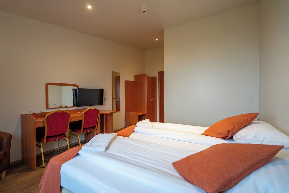 A hotel room with a bed, two red chairs, a desk, a television, and a wardrobe.