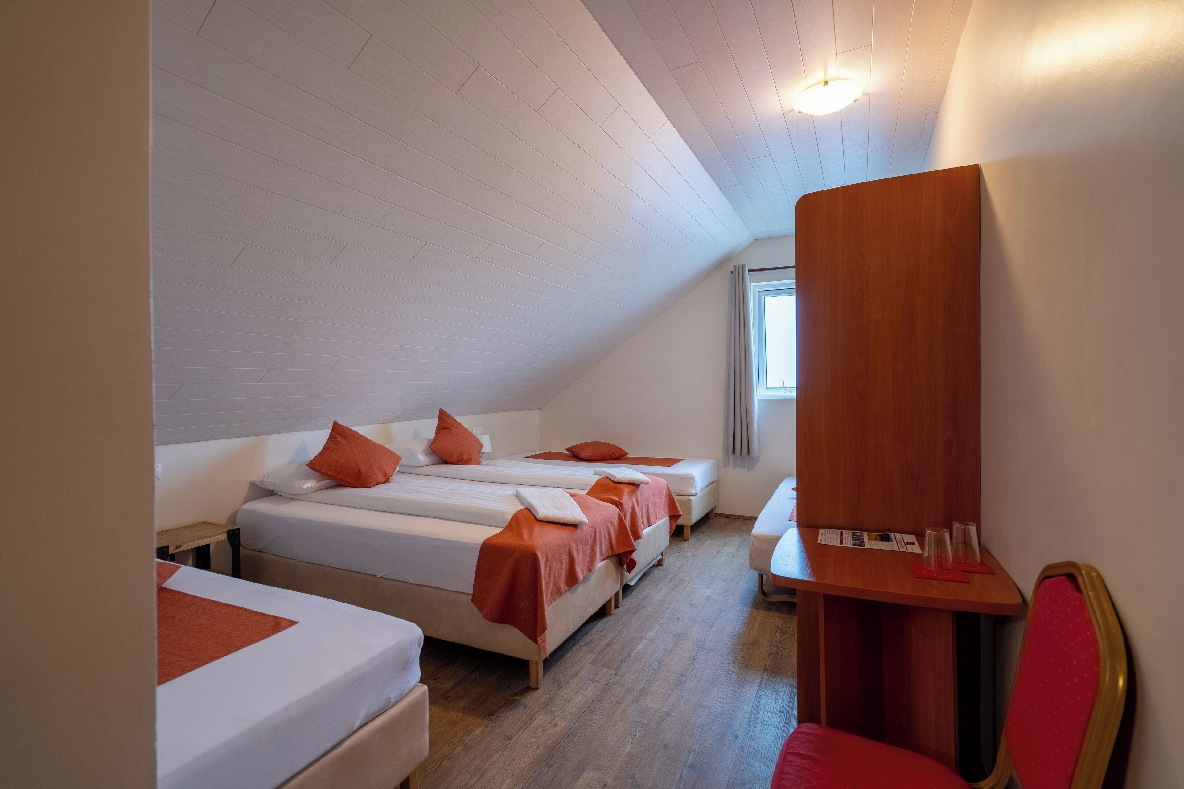A room with three beds aligned against the wall, a wooden desk, and a chair.