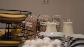 A breakfast buffet with labeled containers of cereal and milk, and a banana stand.