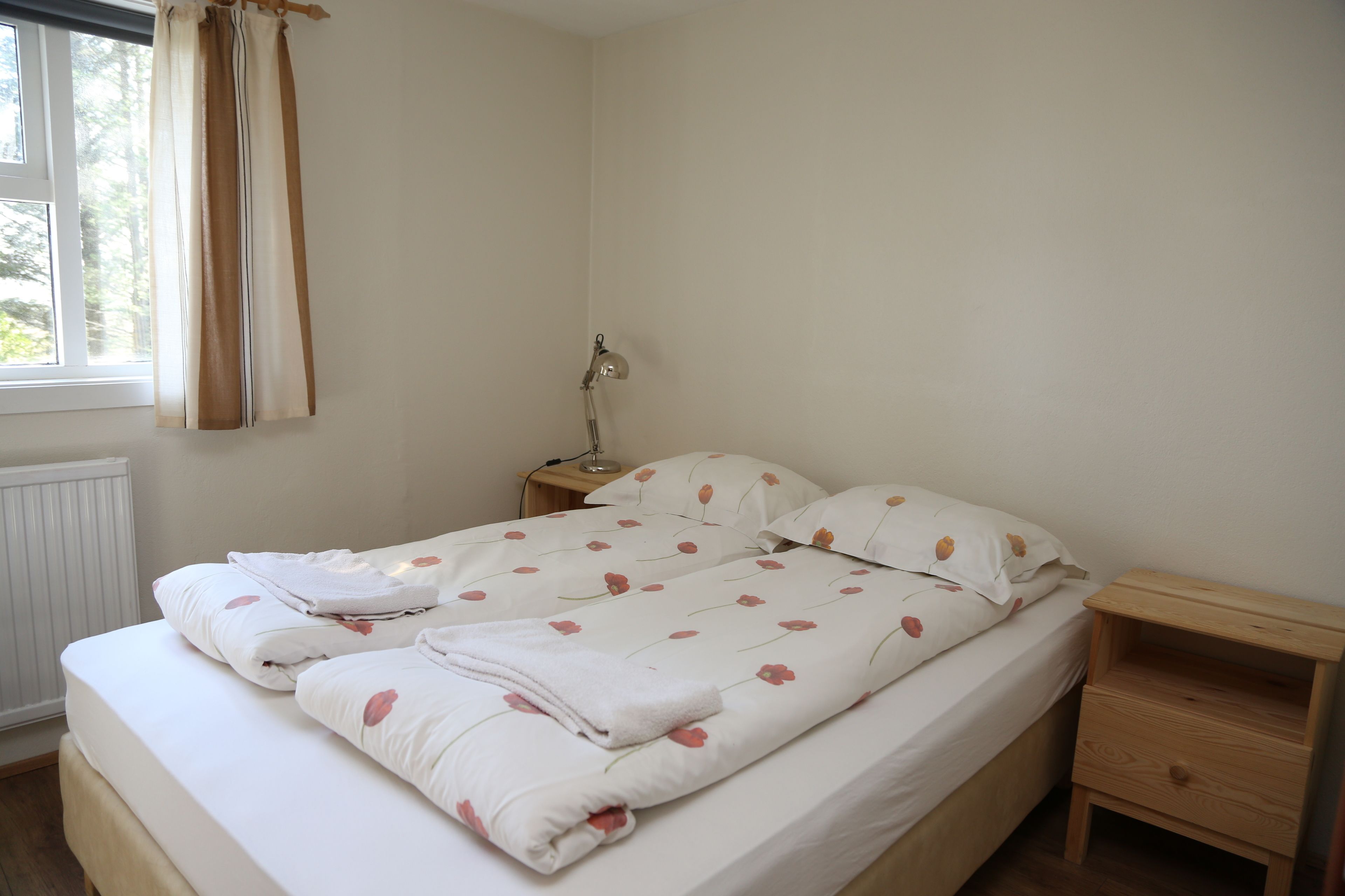 A neatly made bed with a floral duvet cover, a bedside lamp, and a wooden nightstand.