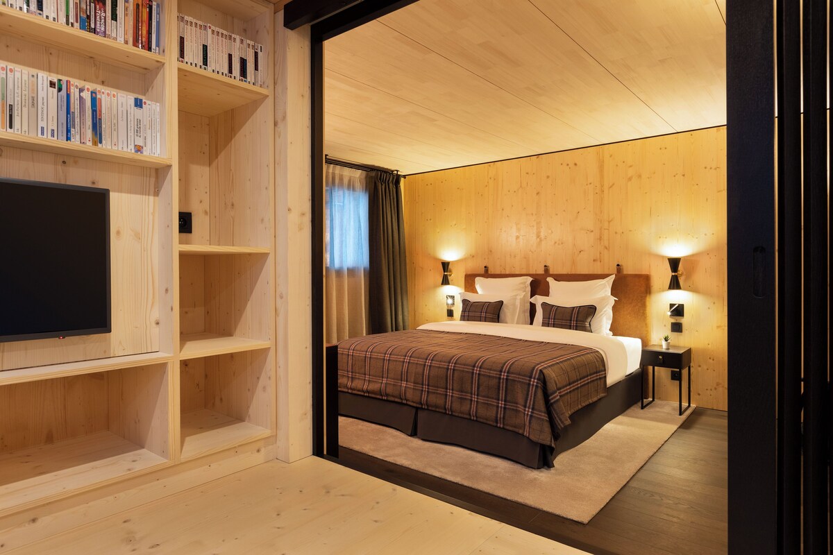 Un dormitorio con una cama grande, televisión, estanterías de madera y dos lámparas de noche.