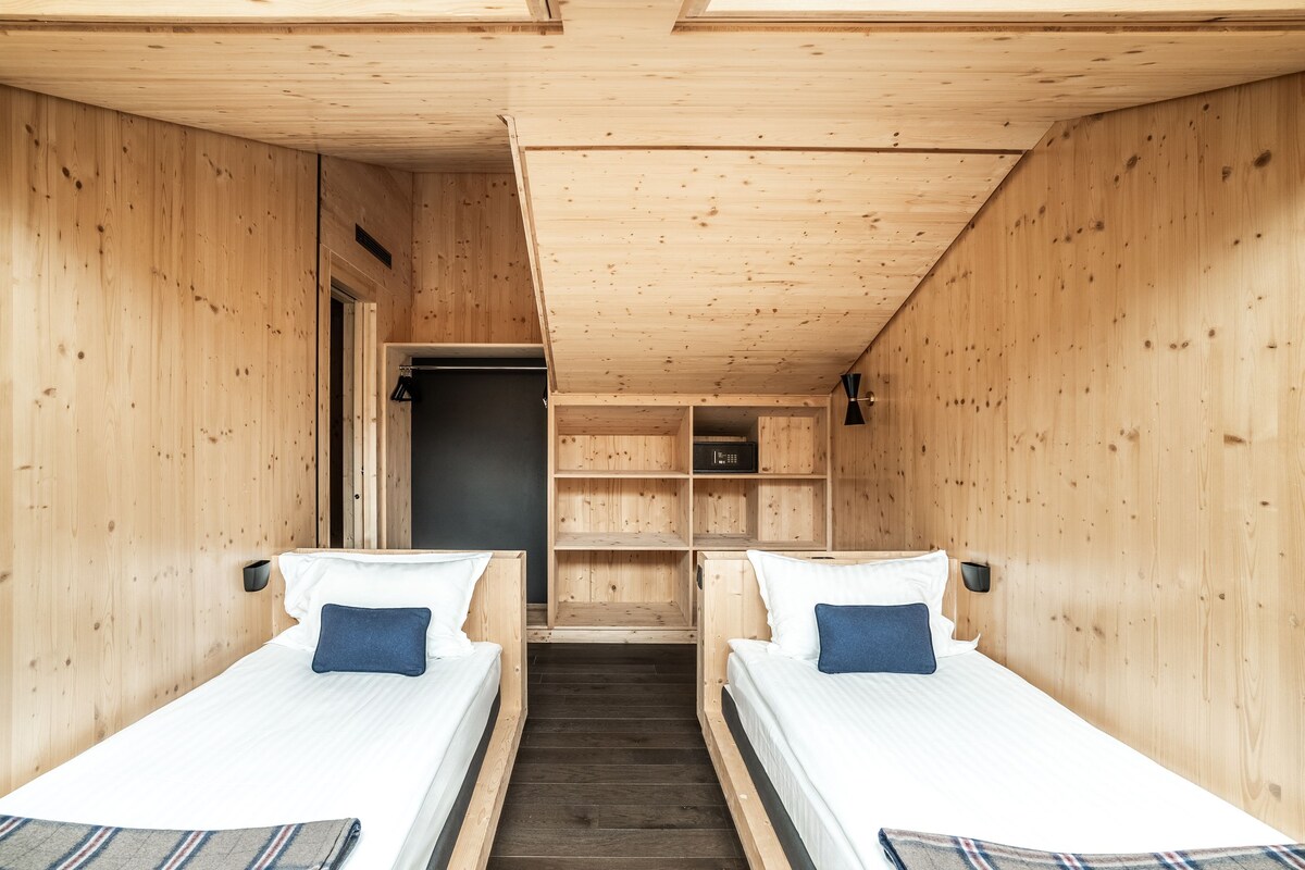 Una cabaña de madera con dos camas individuales, un armario pequeño y una estantería.