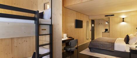 Habitación de hotel con literas, un escritorio, una silla, una cama con manta escocesa, una mesita con un florero y un televisor montado en la pared.