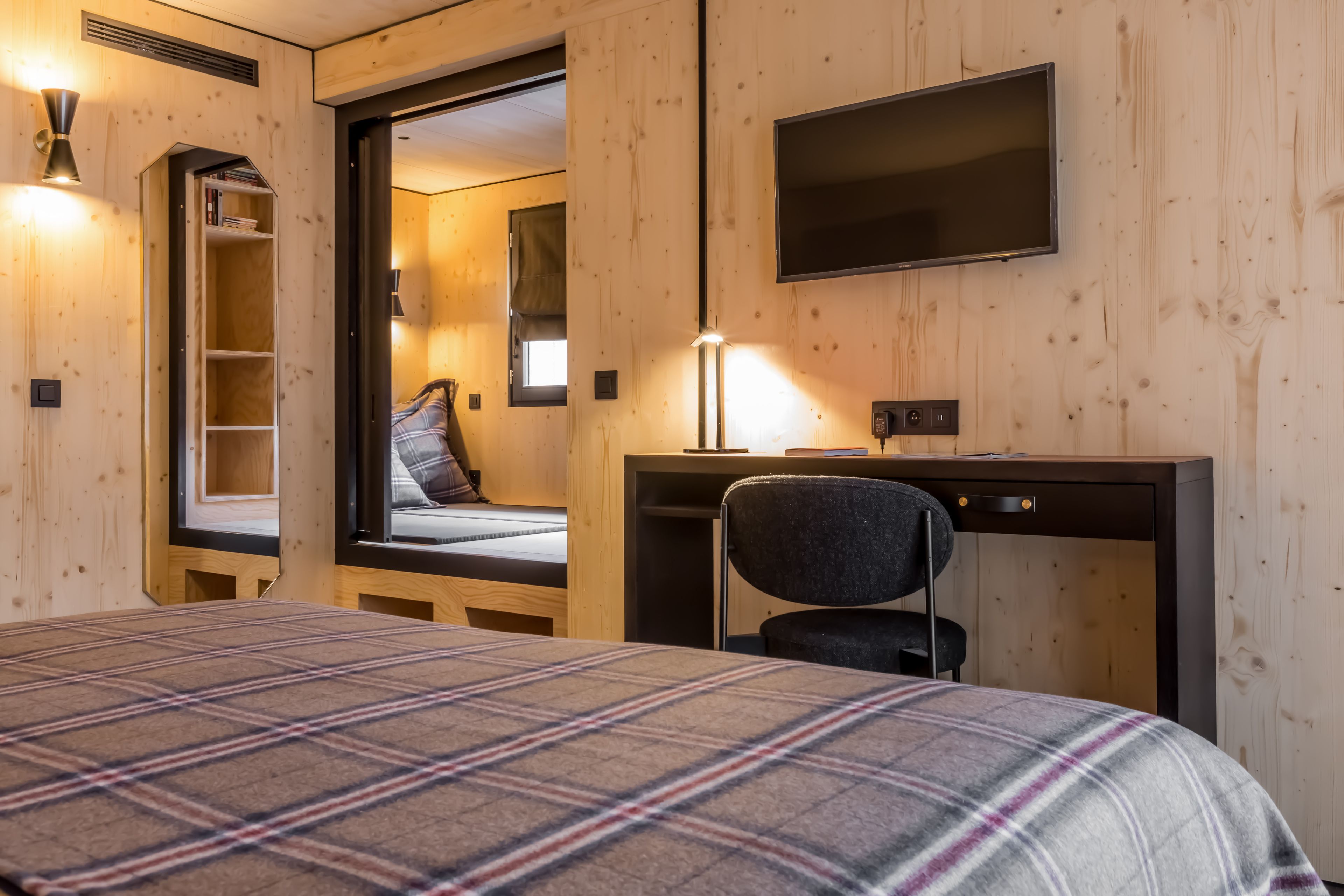 A bedroom with a bed, a desk, a chair, a TV, and a window.