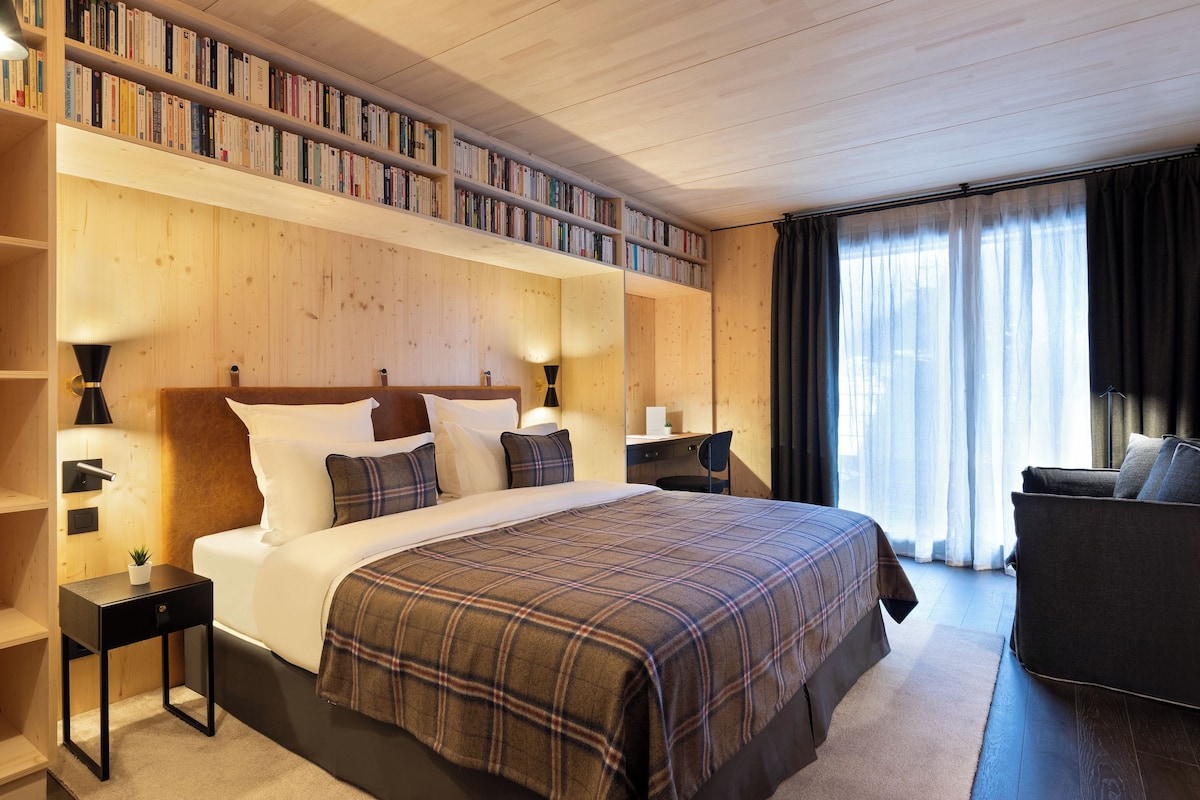 Una habitación de hotel con una cama grande, una estantería, un escritorio y un sofá.
