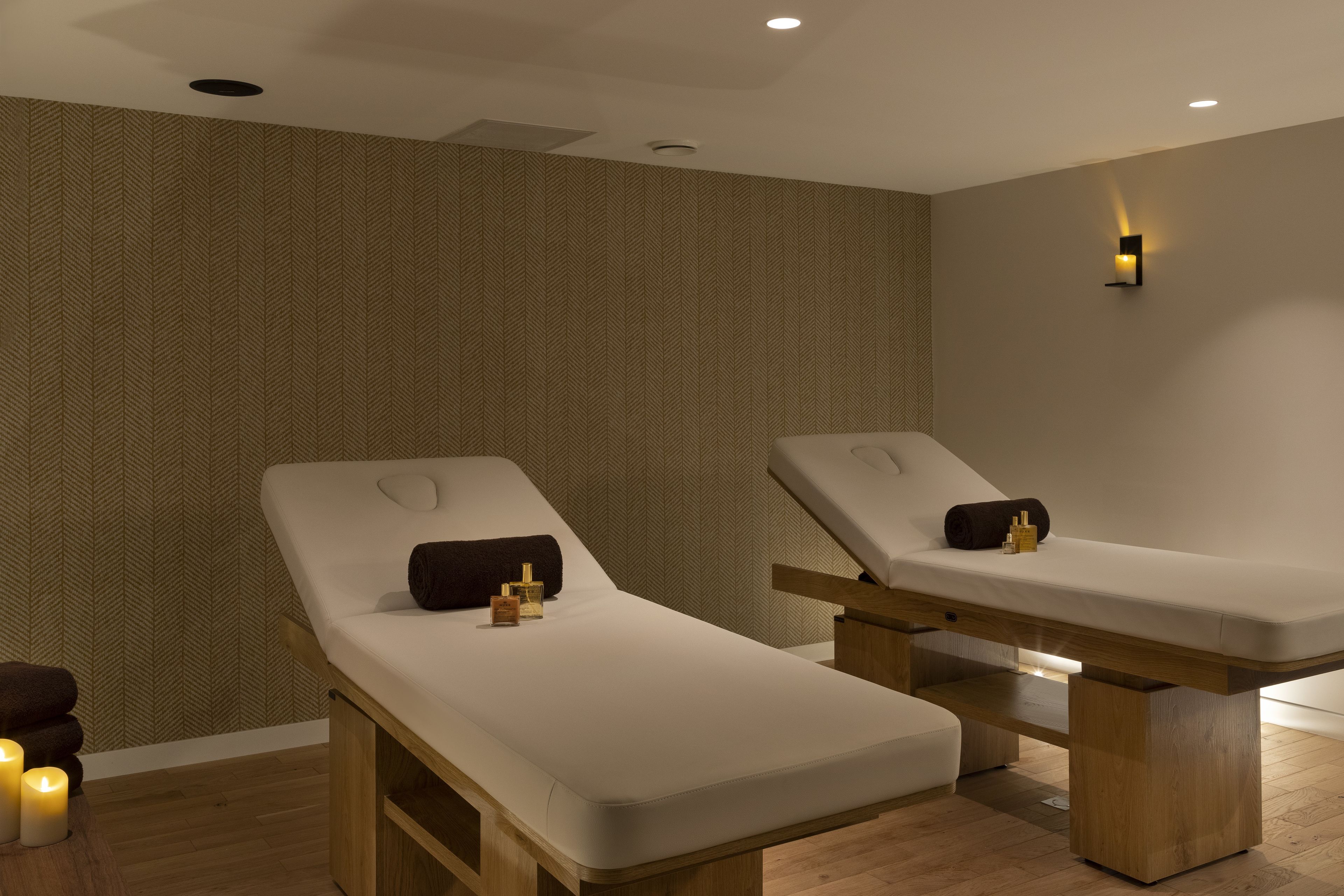 Een spa-ruimte met twee massagetafels, houten banken en kaarsen.