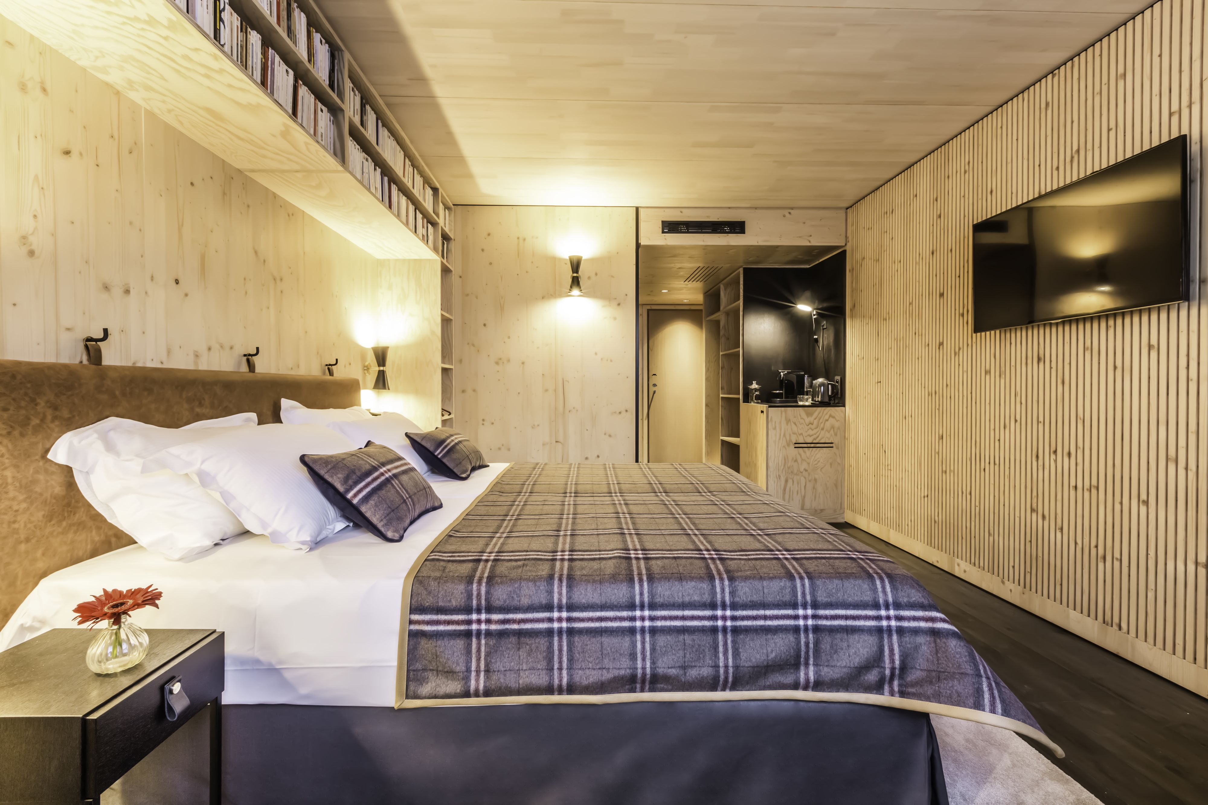 Une chambre d’hôtel moderne avec un grand lit, un téléviseur à écran plat fixé au mur et une bibliothèque en bois.