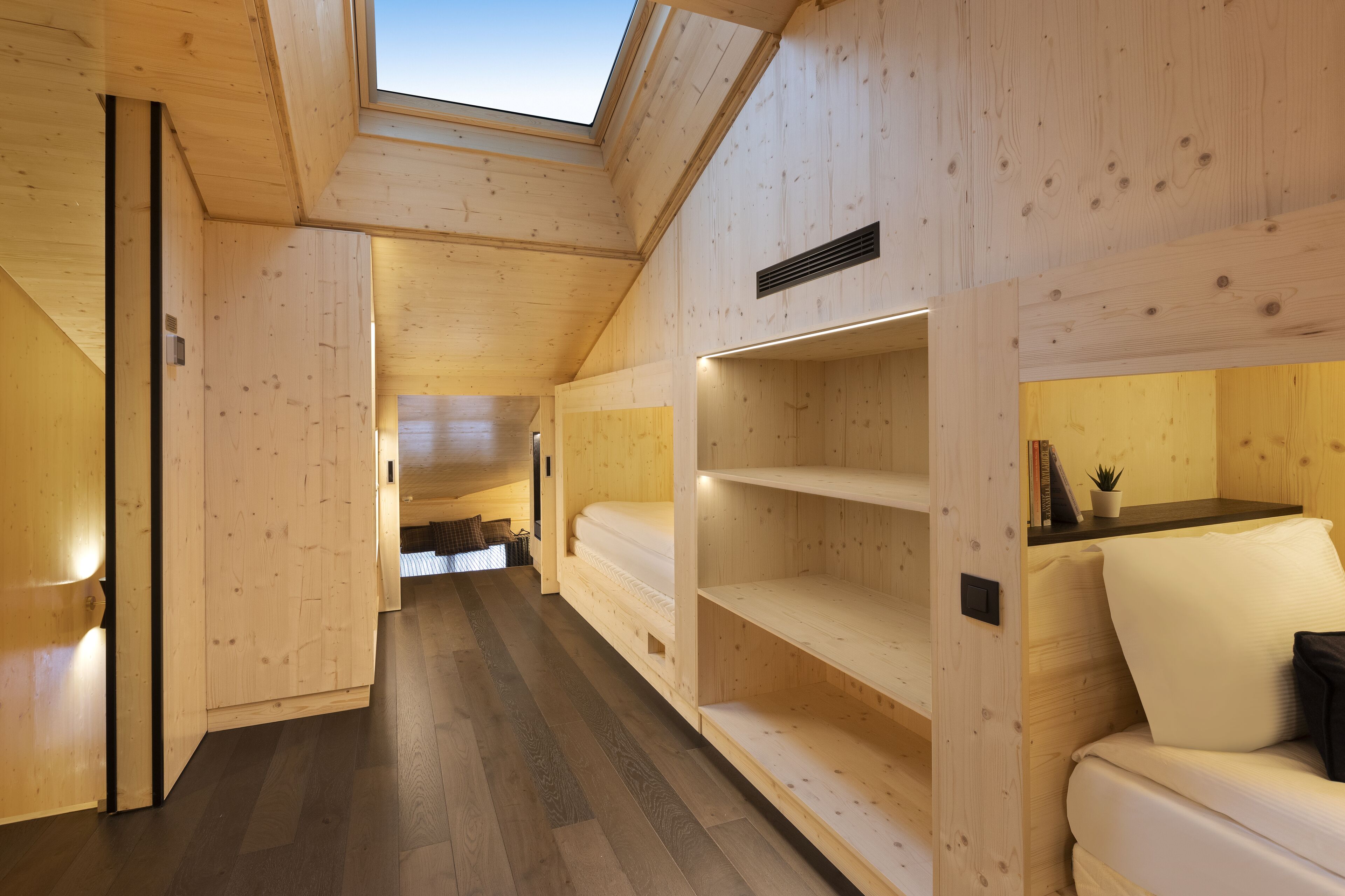 A wooden interior with a skylight, a bed, and built-in shelves.