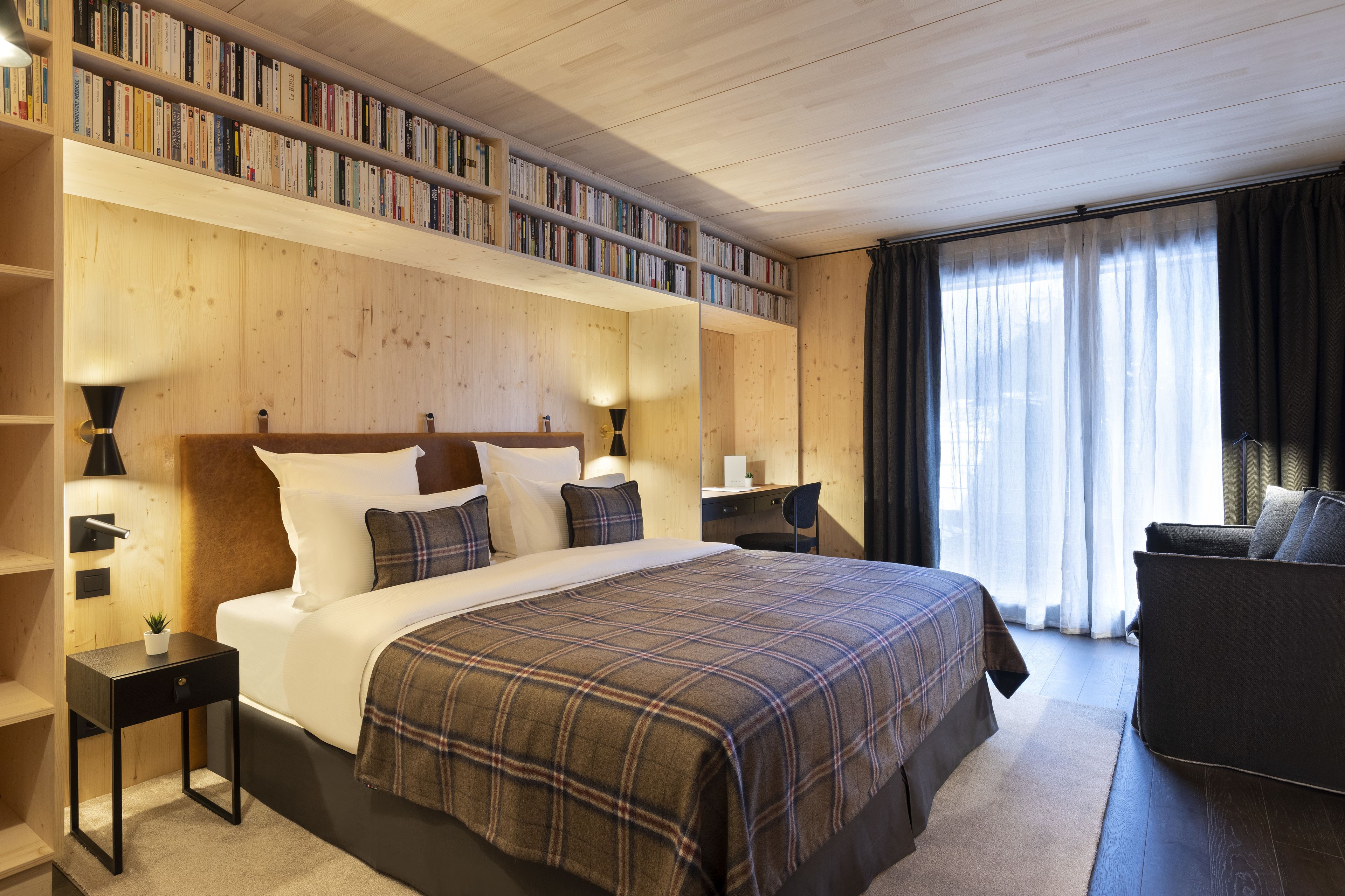 A hotel room with a large bed, a bookshelf, a desk, and a sofa.