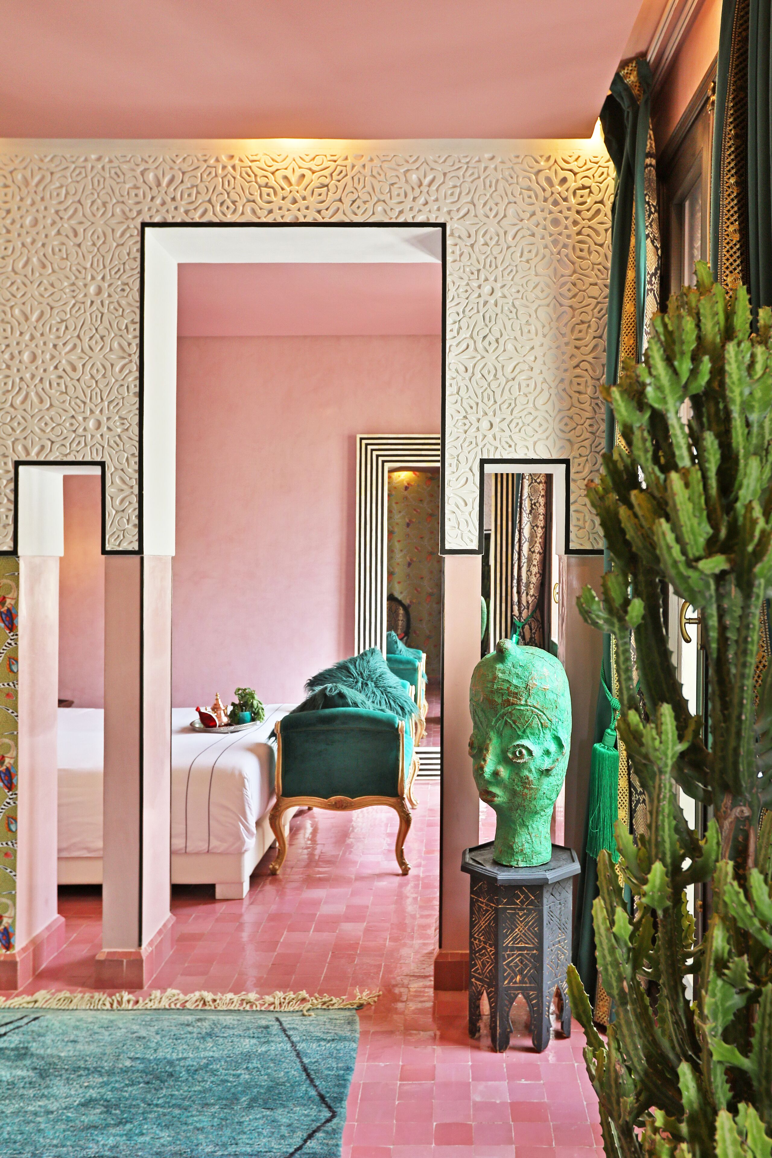 A room with a bed, a green armchair, a cactus sculpture, and a patterned wall.